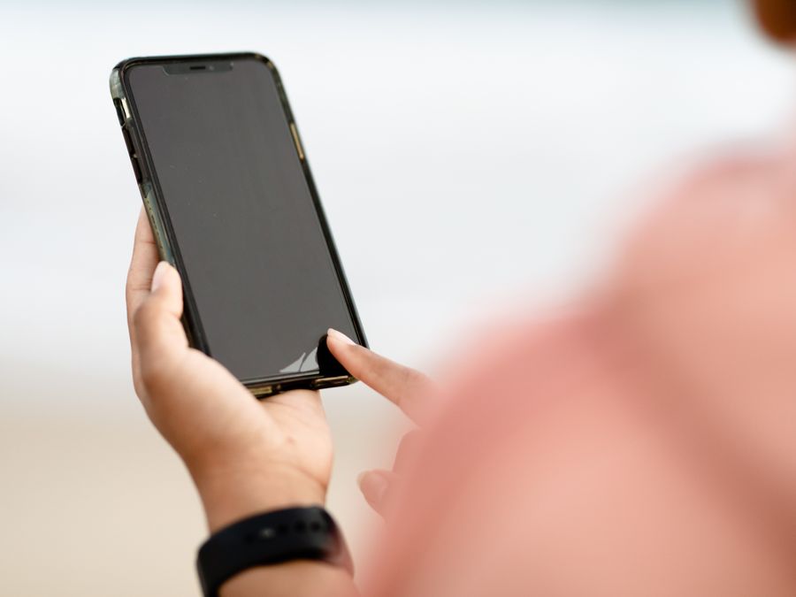 A hand interacting with a smartphone touchscreen outdoors. Modern technology concept.