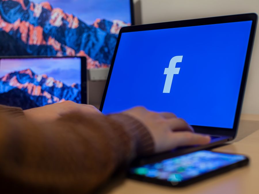 Laptop displaying Facebook at workspace with multiple devices, highlighting modern technology.