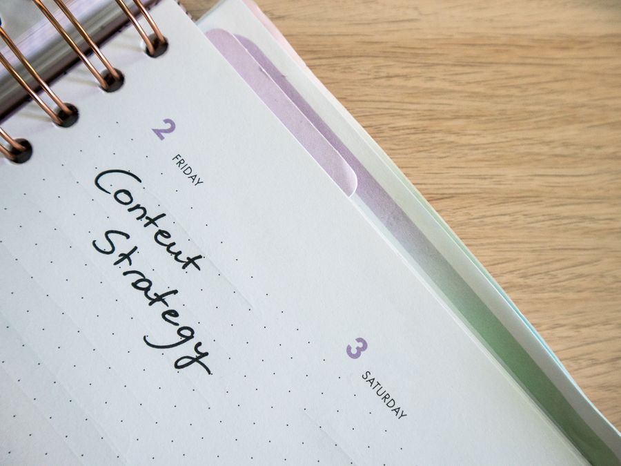 Top view of a notebook open to a day planner featuring 'Content Strategy' handwritten, lying on a wooden desk.