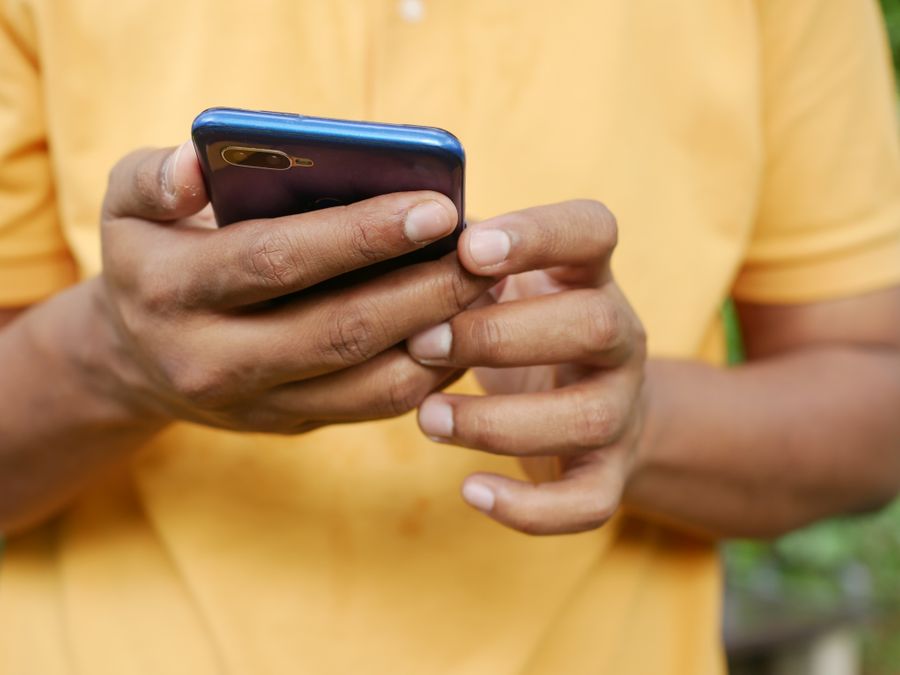 Close-up of a person in an orange shirt using a smartphone outdoors.