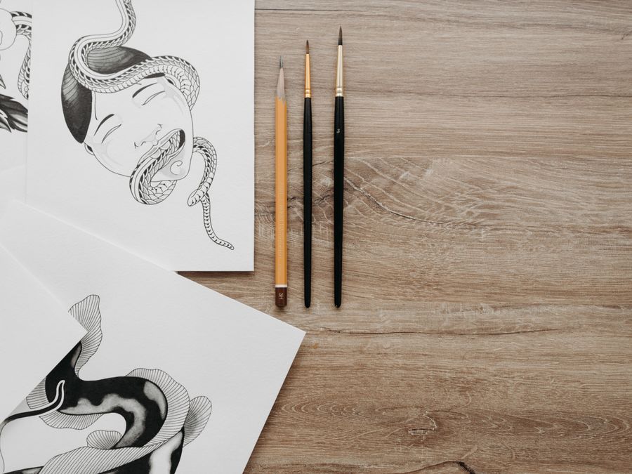 Artistic flat lay featuring pencil sketches and brushes on a wooden surface, perfect for creative content.