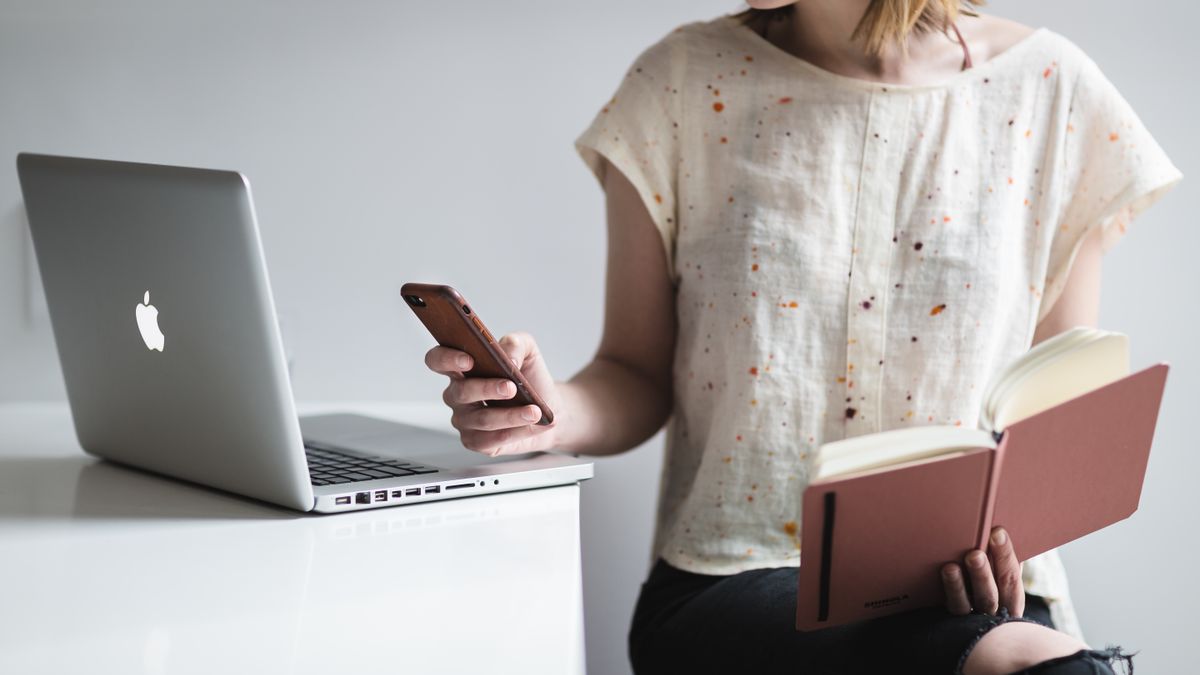 Woman working on a laptop while reading and texting, embodying modern multitasking.