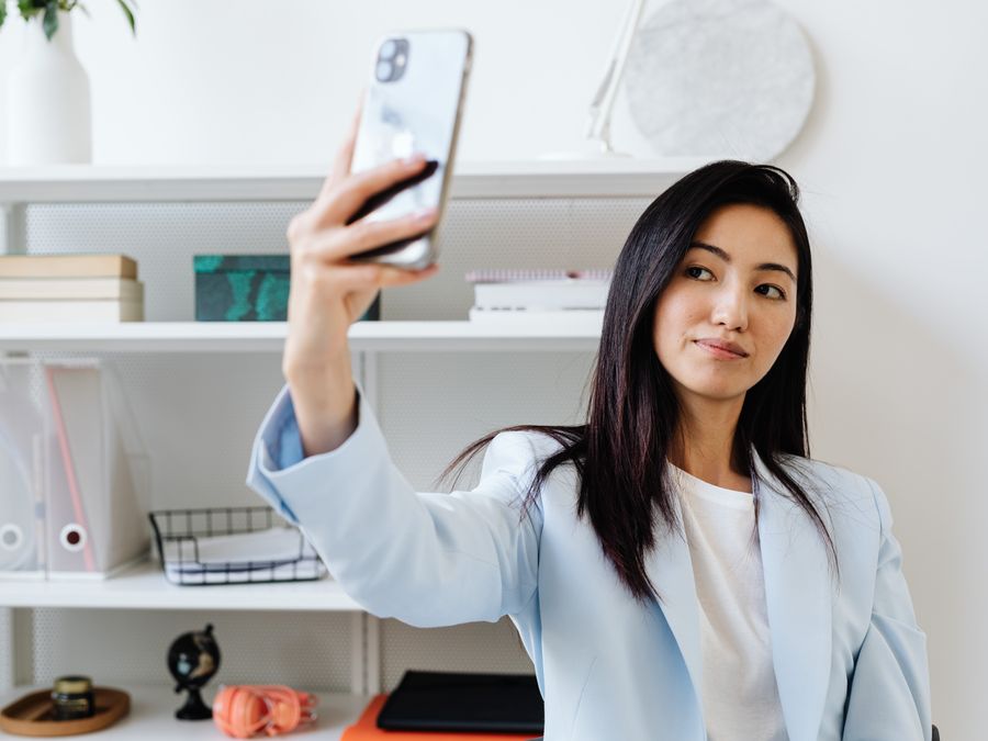 Professional woman in blue blazer capturing a selfie in a modern office setting.