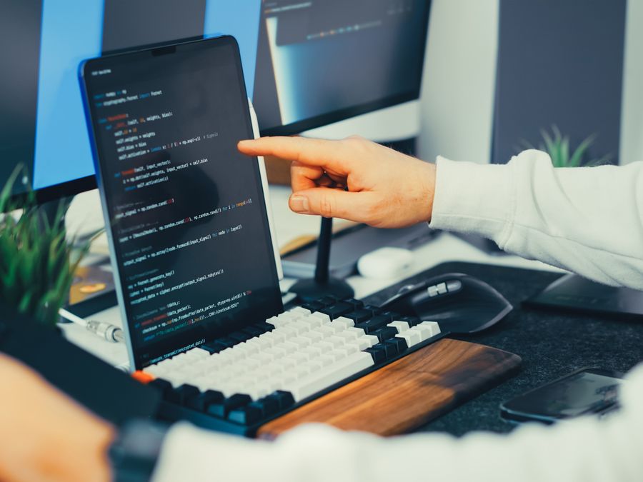 A programmer working on code with a laptop and monitor setup in an office.
