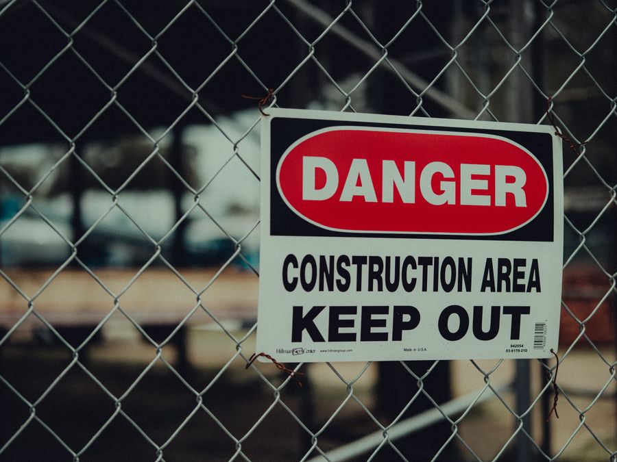 Close-up of a warning sign on a chain link fence at a construction site indicating danger.