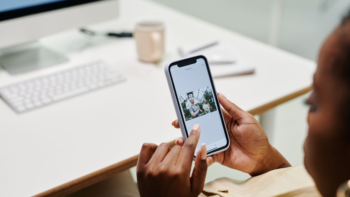 Close-up of hands using a smartphone at a desk with a computer. Ideal for tech and lifestyle content.