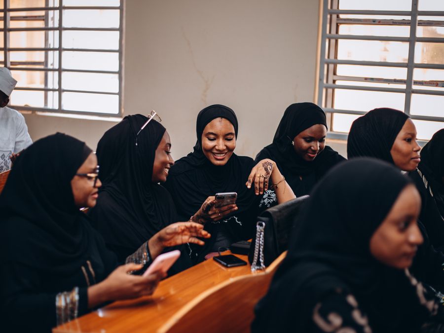 A group of women in hijabs sharing a joyful moment indoors, connected via smartphones.