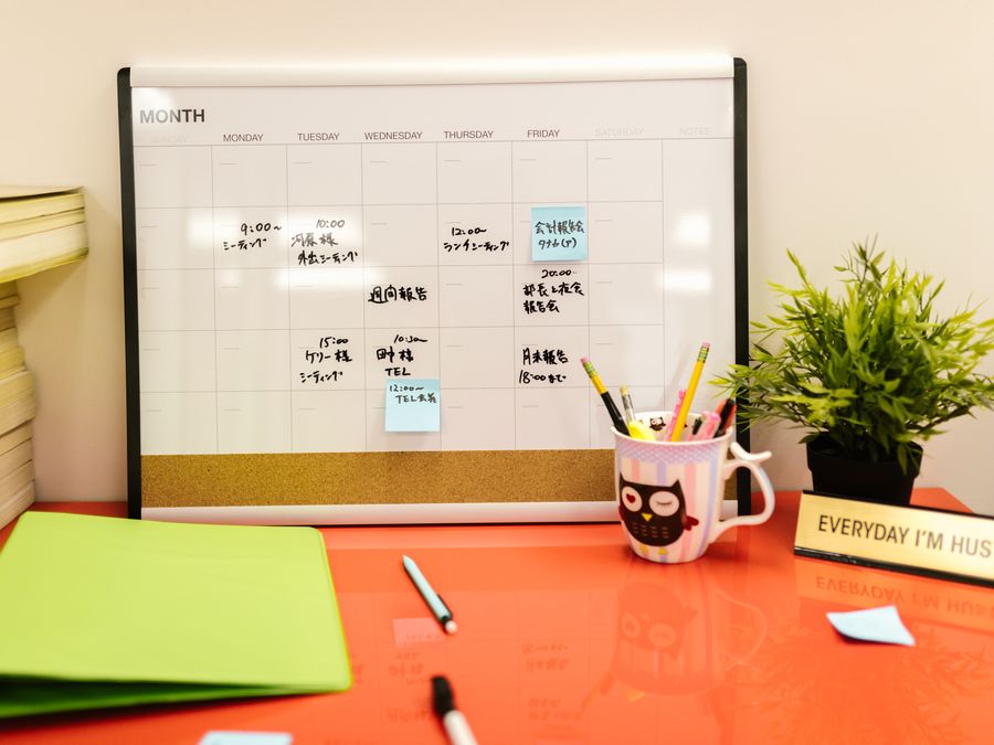 Neat workspace with a calendar, plant, and stationery on a red desk.
