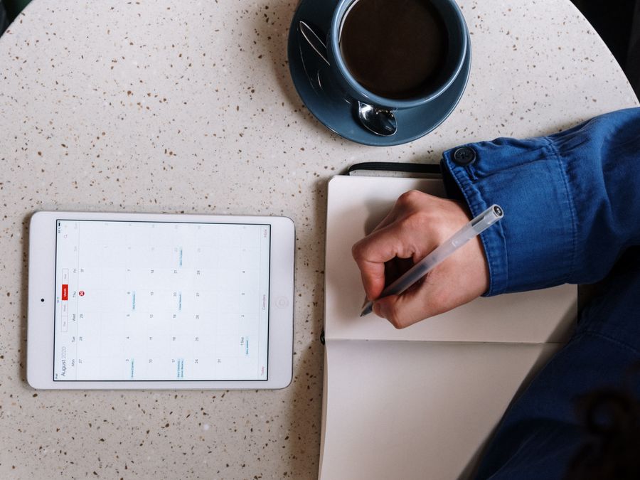 Overhead view of planning with a tablet, notebook, and coffee on a table.