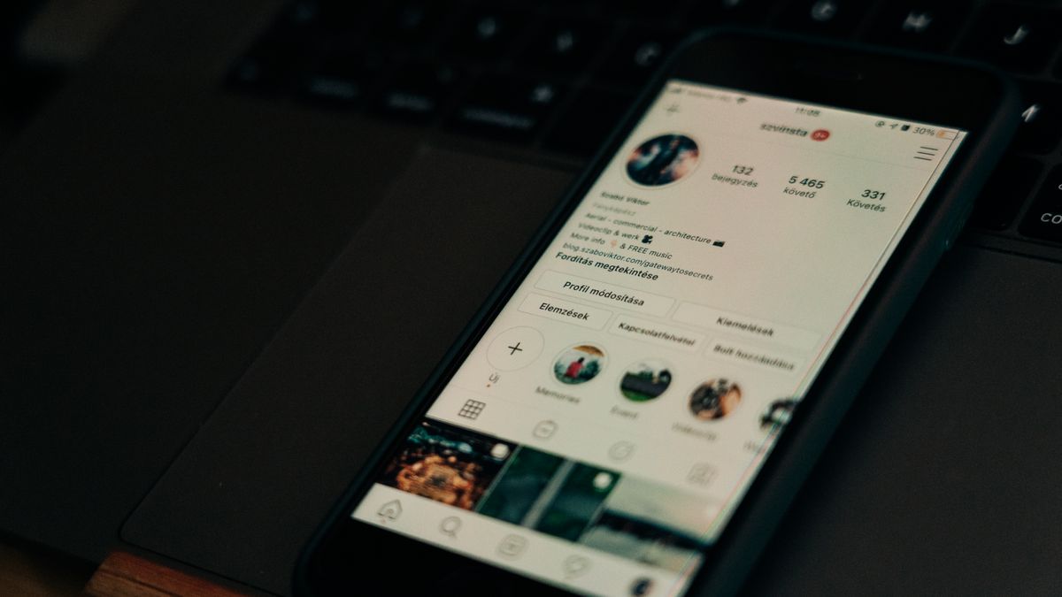 Close-up of smartphone showing a social media profile screen next to a laptop.
