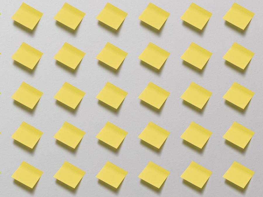Flat lay of yellow sticky notes arranged in a grid pattern on a white surface, perfect for business or school themes.