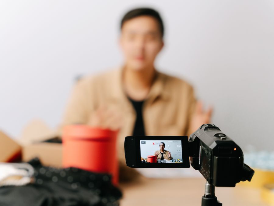 A blogger sits in front of a camera for filming a video indoors.