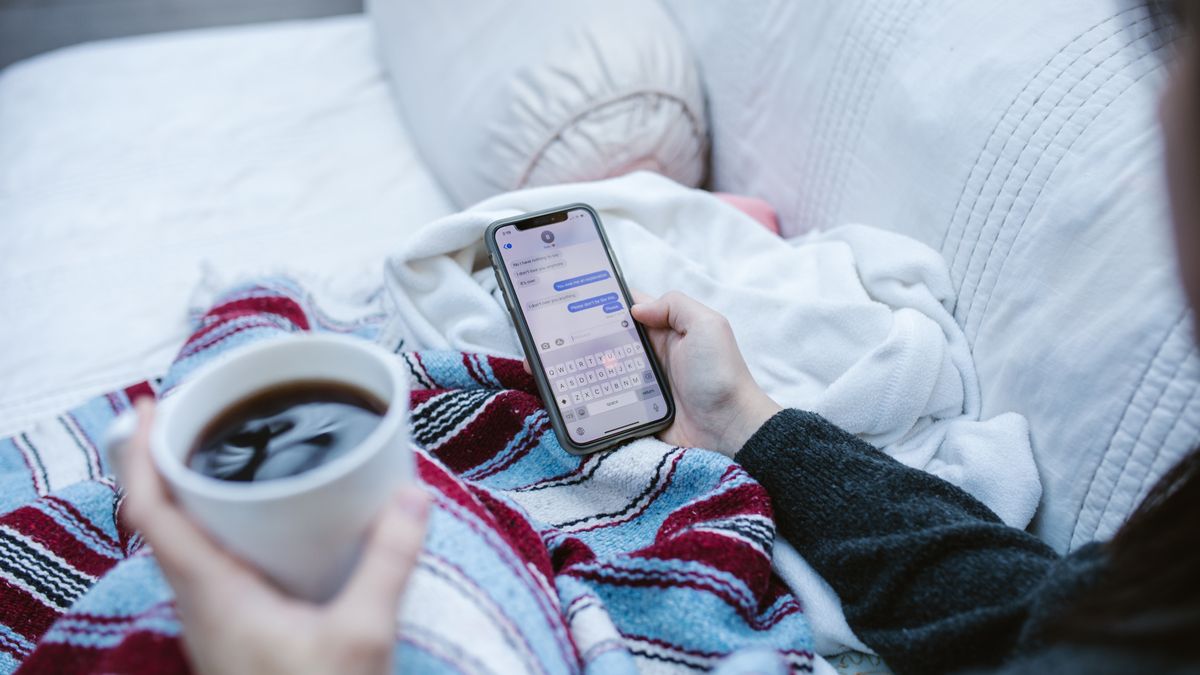 Person relaxing indoors with coffee and smartphone, texting in a cozy setting.