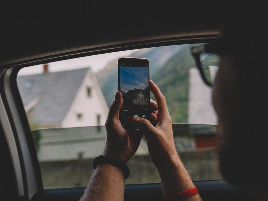 Person takes photo of scenic view from car window with smartphone in Norway.