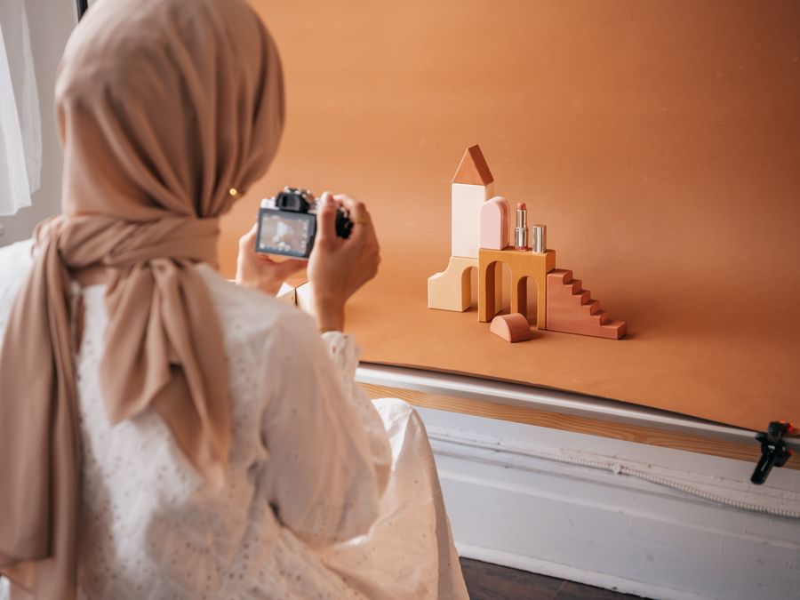 A woman takes a photo of beauty products with a camera in a studio setting. Neutral colors.