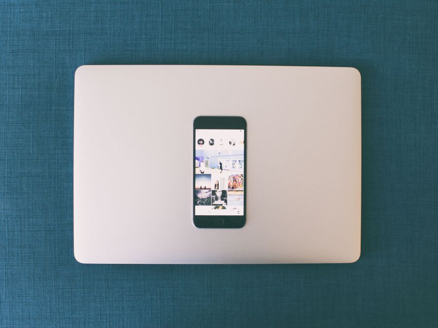 Flat lay of a smartphone on a laptop with social media photos on screen.