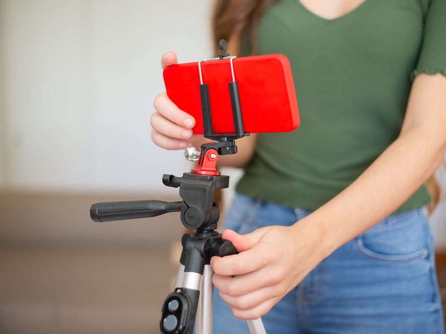Female adjusting smartphone onto tripod for recording indoors.