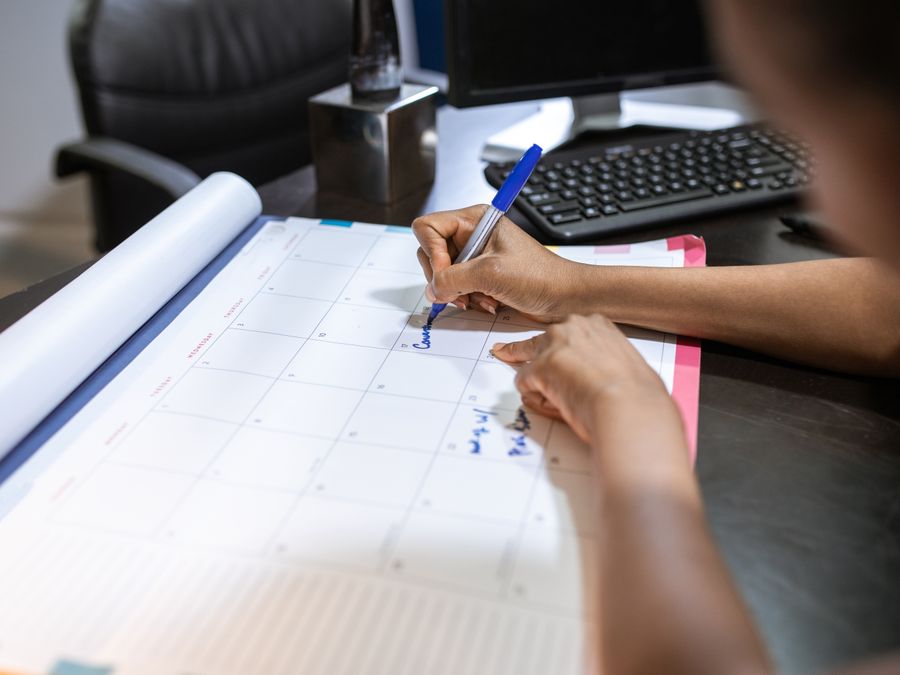 Close-up of a woman planning her schedule on a desk calendar in an office setting.
