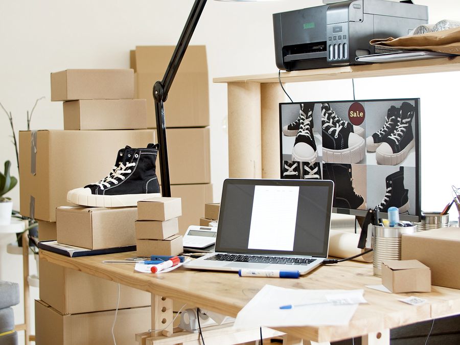 A busy workspace with sneakers, boxes, and a laptop indicating an online shoe store or e-commerce setup.