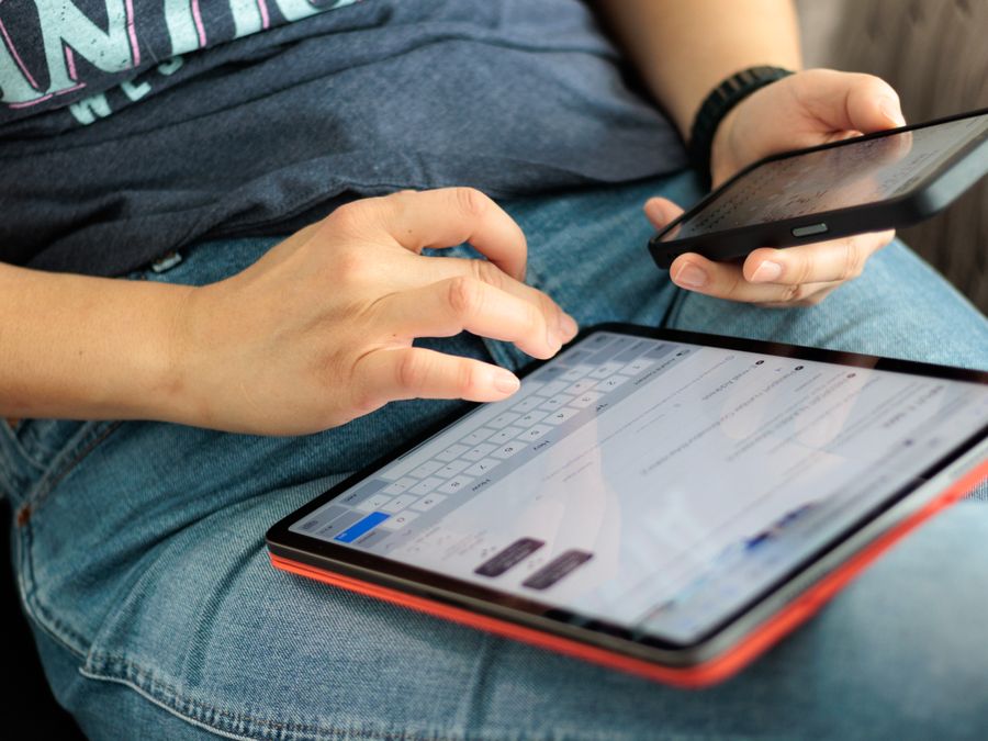 Close-up of adult using a tablet and smartphone indoors, showcasing digital connectivity and multitasking.