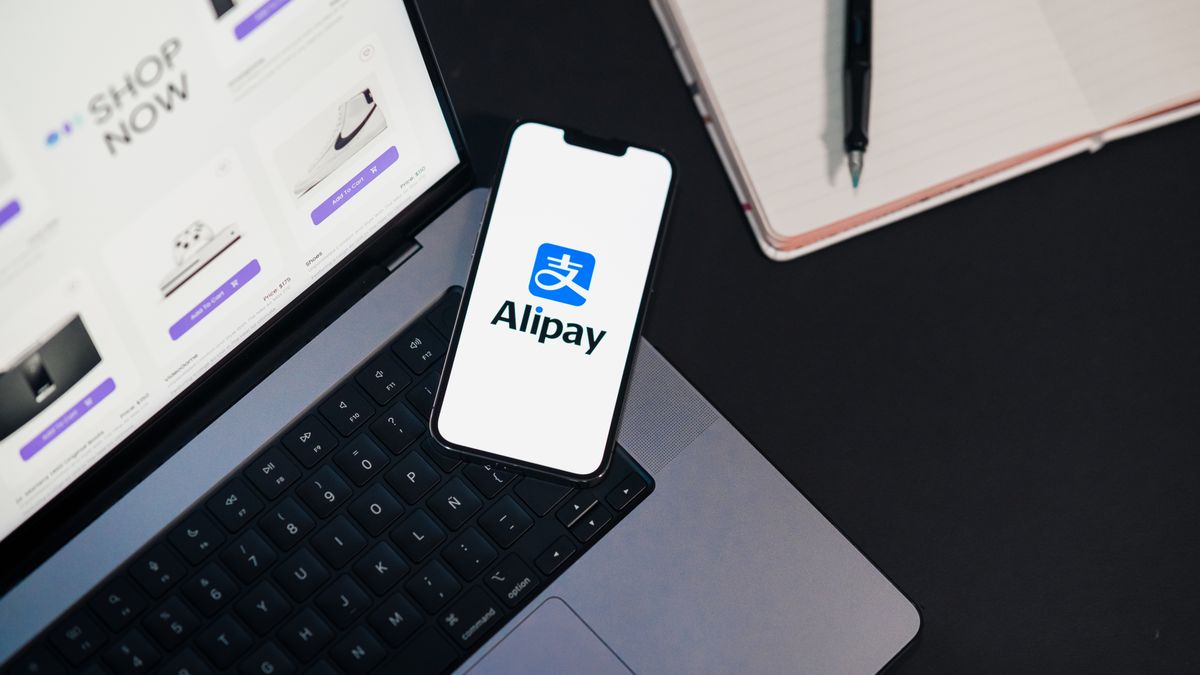 Smartphone displaying Alipay app on open laptop with online shopping site.