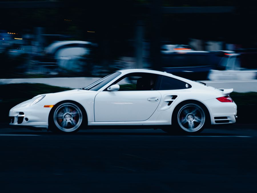 Dynamic shot of a white sports car driving fast on a city street at night, showcasing speed and style.