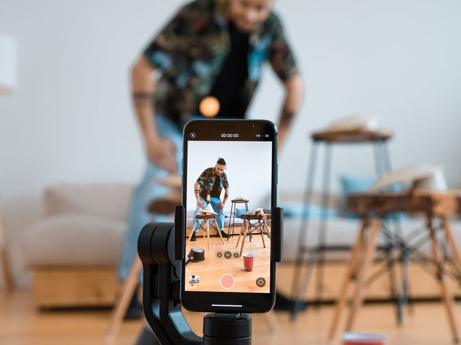 Man recording video content with smartphone on a tripod in a cozy living room.