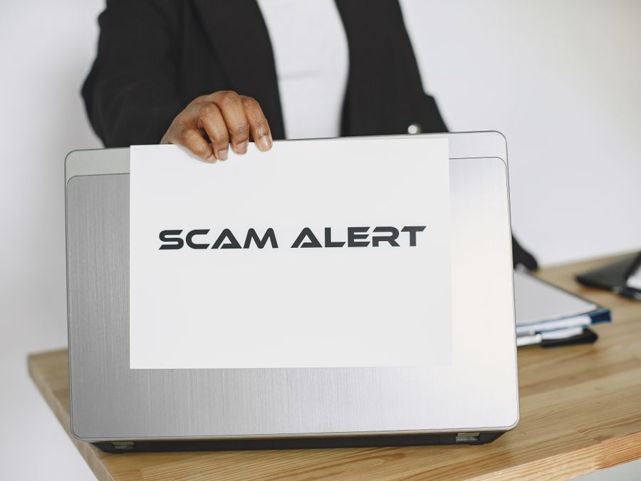 Business person holding a scam alert sign over a laptop, warning against online fraud.