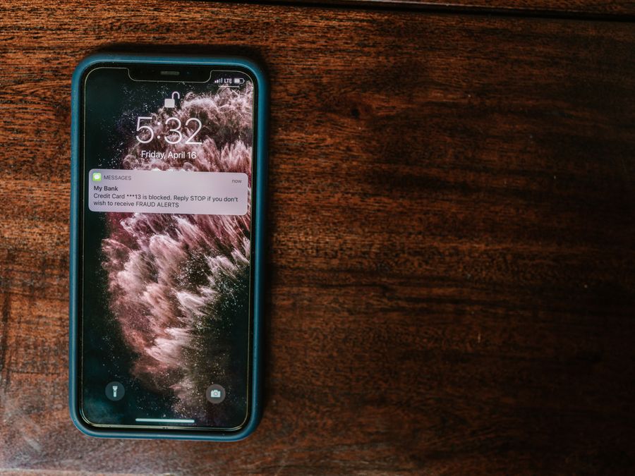 Close-up of smartphone on wooden surface displaying a bank alert message.