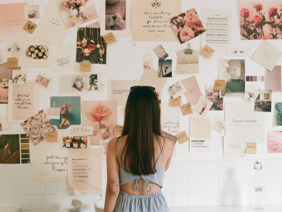 A woman with tattoos looks at a creative mood board filled with floral photos and quotes.