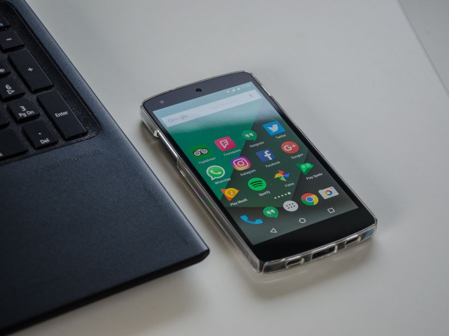 Smartphone on a table showing various social media apps beside a laptop keyboard.