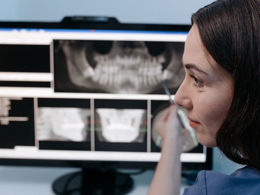 Female dentist reviewing digital dental x-rays on a computer screen in a clinic setting.