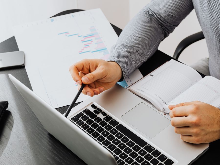 Professional using laptop and reviewing documents at office desk for data analysis.