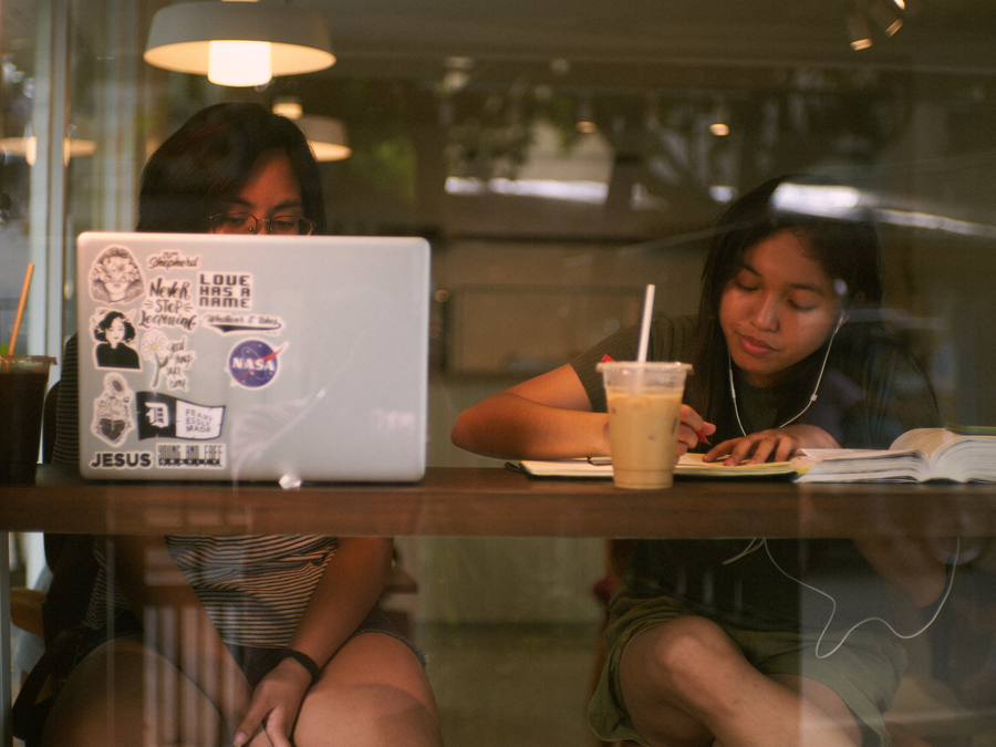 Two women engaged in study and work at a coffee shop, using a laptop and notepad.