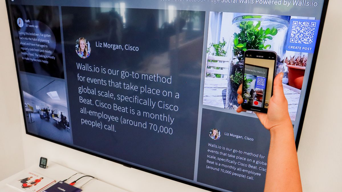 A person uses a smartphone to scan a QR code displayed on a large screen indoors.
