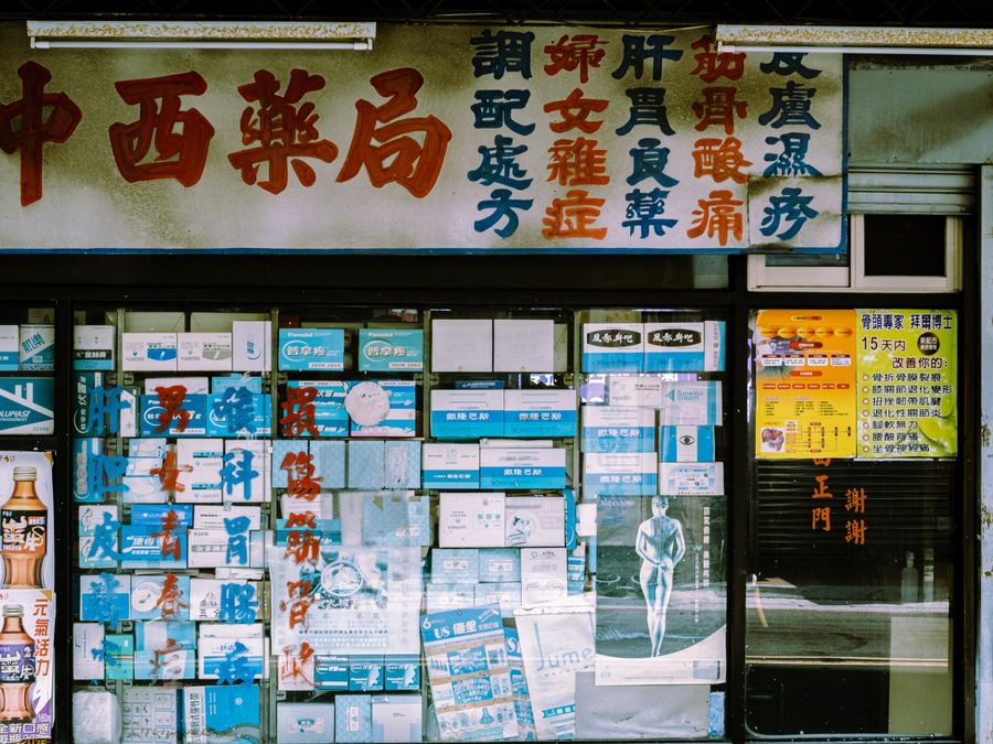 A traditional storefront with Asian script and various posters displayed in the window.
