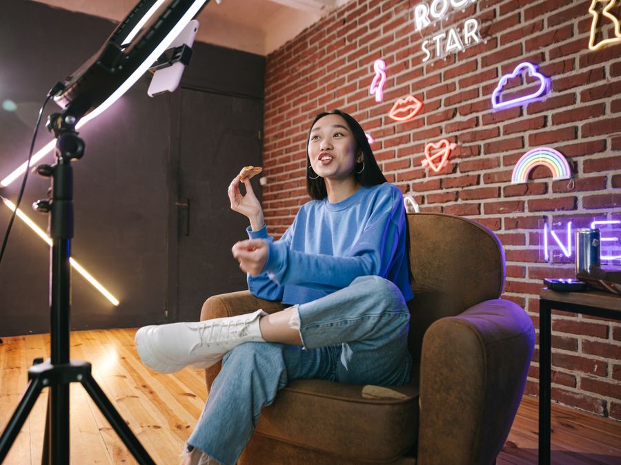 Young Asian woman streaming live indoors with neon lights, engaging audience through technology and creative content.