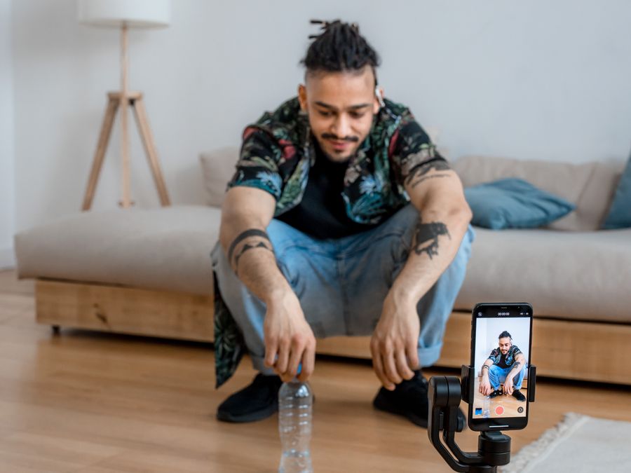 Young man recording content in living room with smartphone on a tripod.