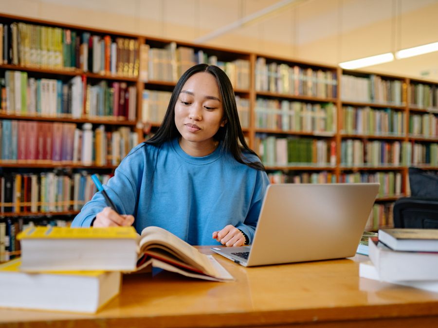 Young woman studying in a library with books and laptop, focusing on education.