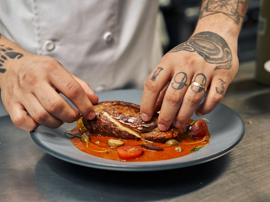 A chef with tattoos skillfully plates a gourmet dish in a professional kitchen.