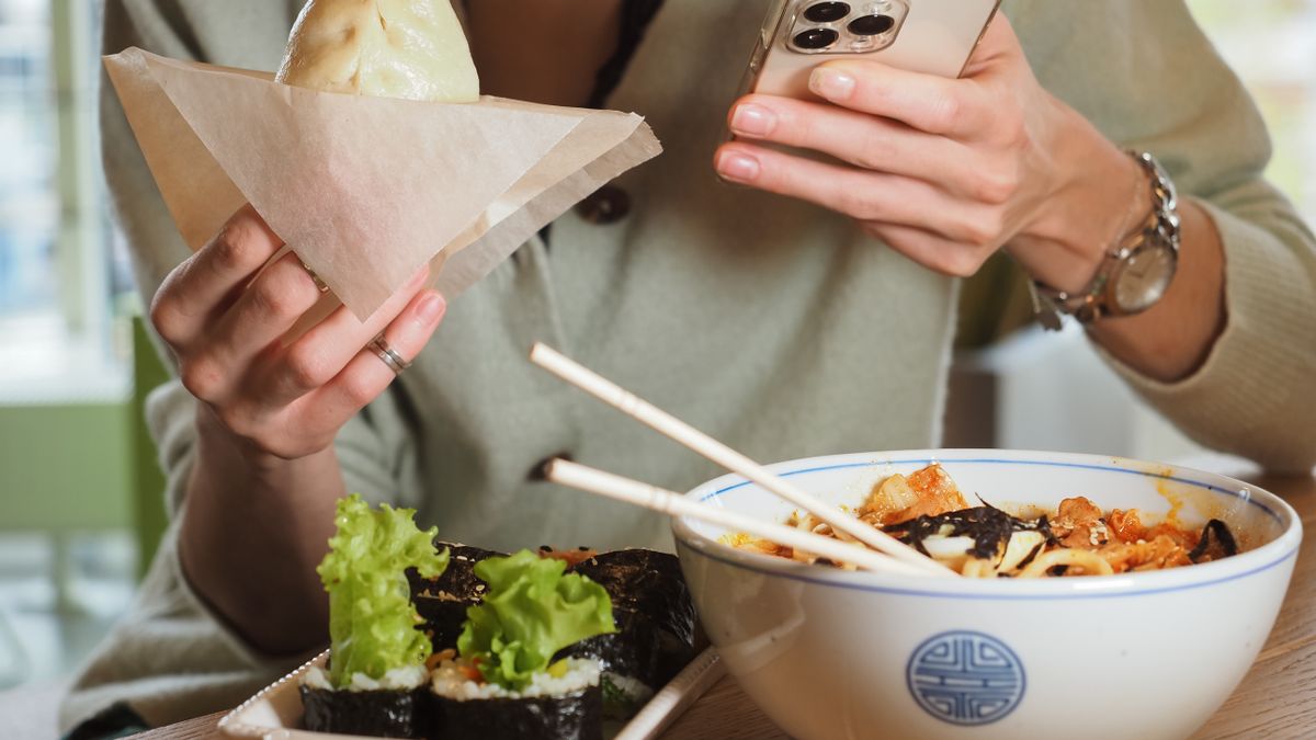 Person enjoying Asian food while using a smartphone at a casual dining setting.