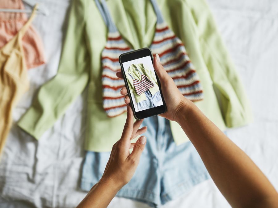 Hands taking photos of trendy outfit using smartphone on bed.