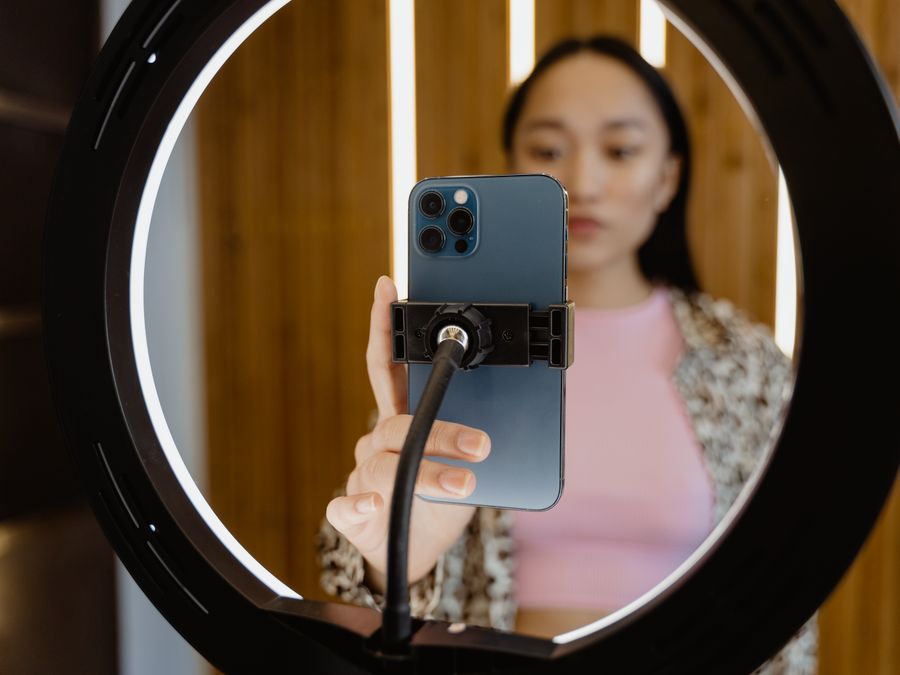 Young woman using a smartphone held by a ring light for video recording indoors.