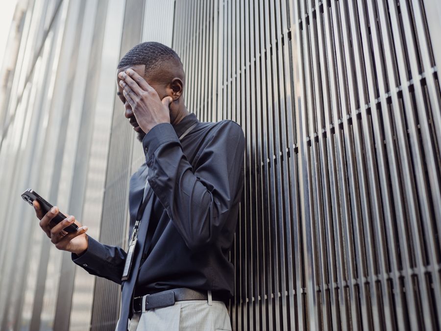 A worried businessman in formal attire using a smartphone outside a modern building.