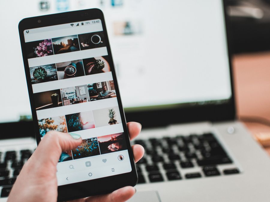 A person uses a smartphone to browse social media in front of a laptop, emphasizing modern technology and lifestyle.