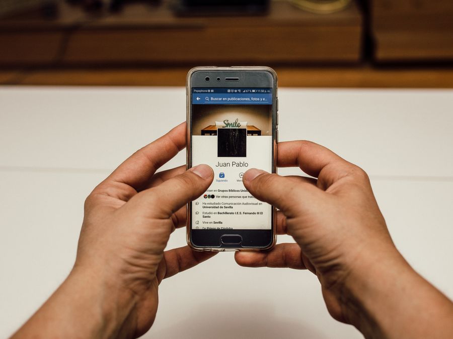 Close-up of hands using a smartphone with a social media page indoors.