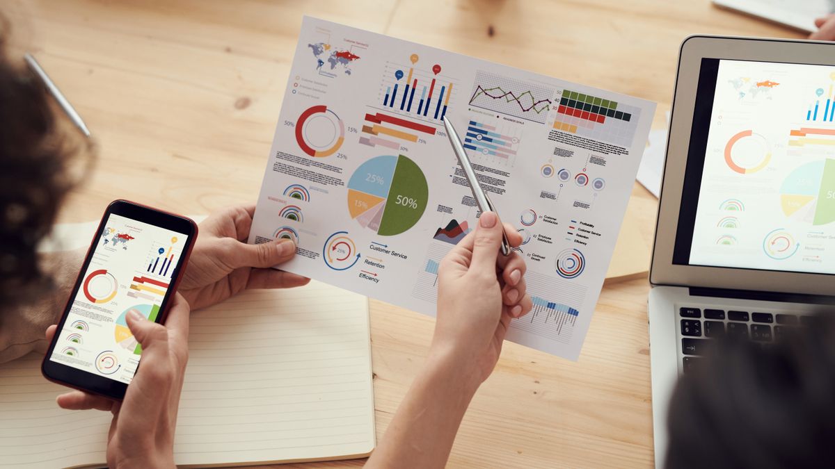 Team members analyze charts during a business meeting with laptops and smartphones.
