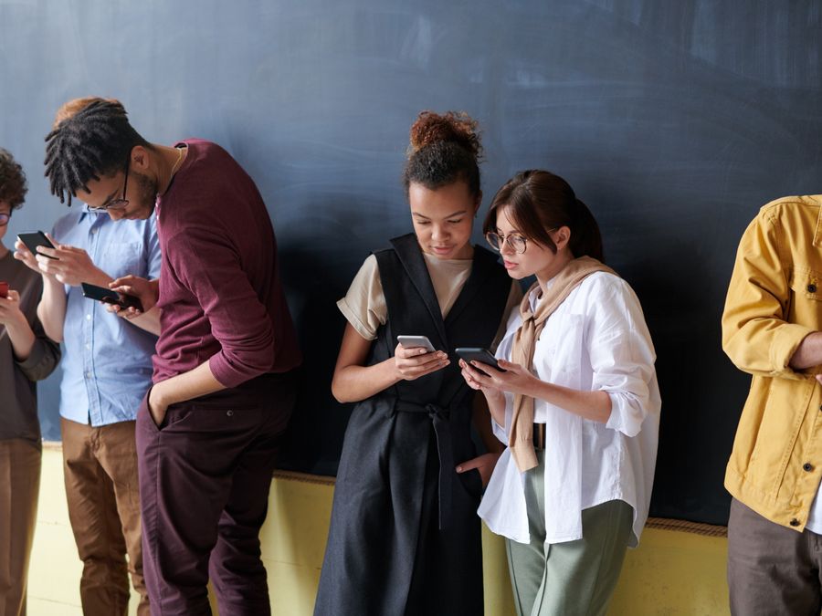 A diverse group of young adults using smartphones in a casual indoor setting.