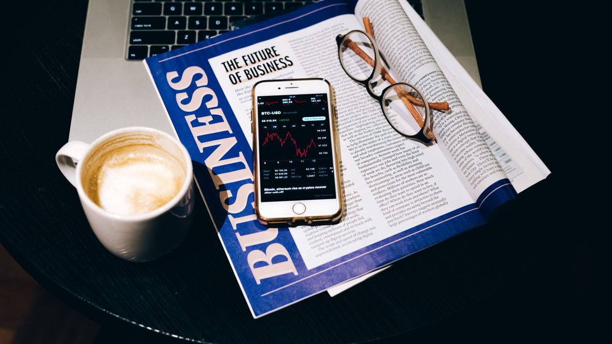 A business setup with a laptop, coffee, phone, and newspaper. Perfect for finance themes.