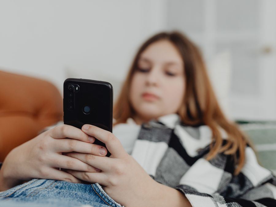 Teenage girl using smartphone while relaxing on a sofa, depicting leisure and connectivity.